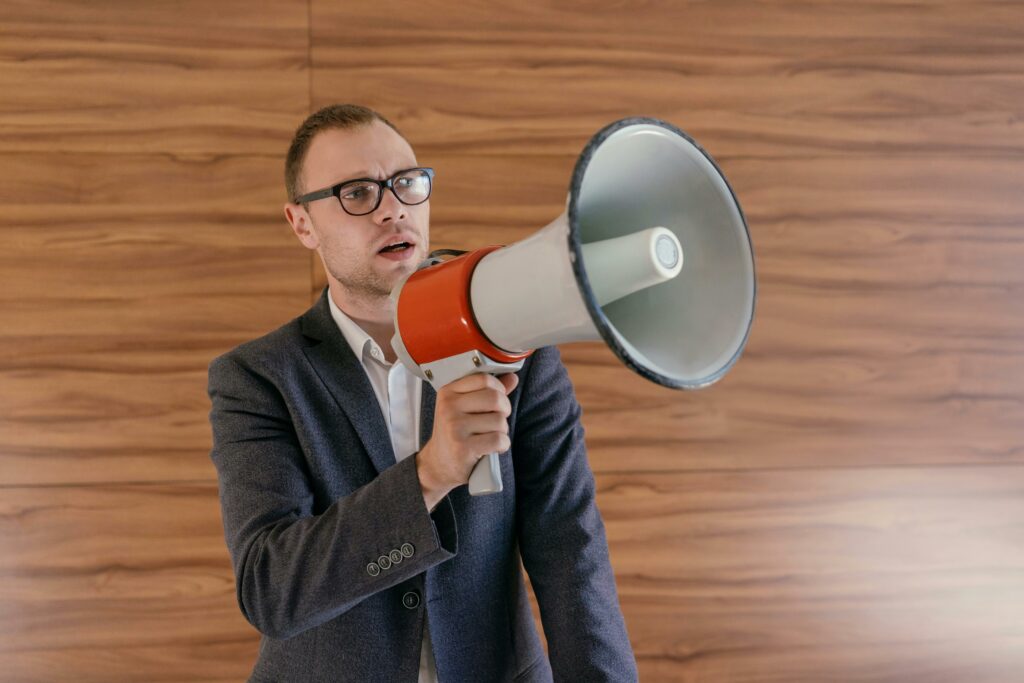 Man in suit holding a megaphone, making a public announcement indoors.